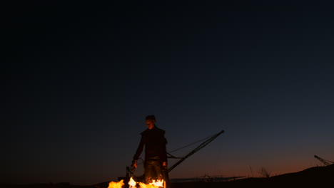 A-man-in-a-raincoat-with-two-flamethrowers-lets-out-a-fiery-flame-standing-at-sunset-on-the-sand